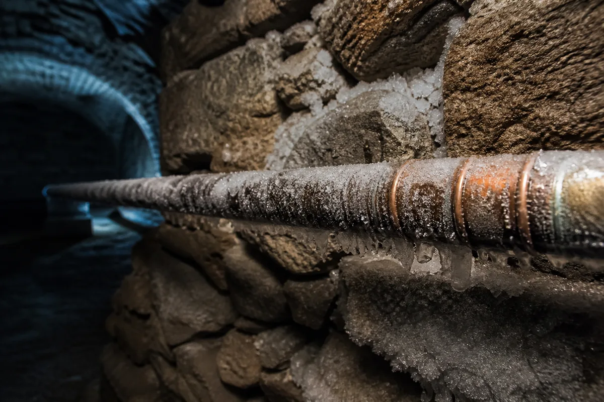 Canalisation en cuivre givrée le long d’un mur en pierre dans une cave voûtée